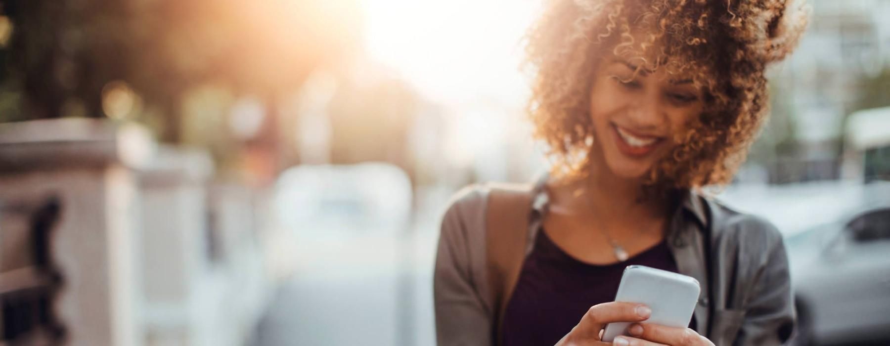 woman texts on her phone as she walks through the city